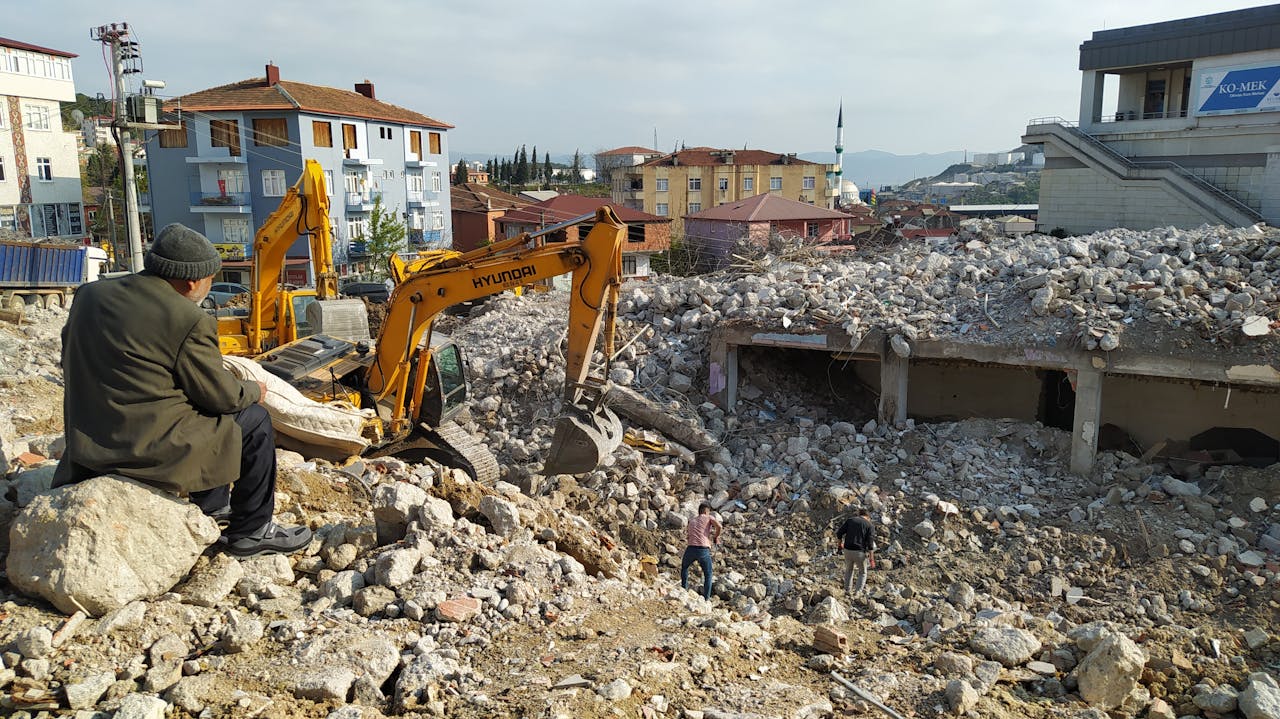 An elderly man observes bulldozers clearing building rubble in Dilovası, Türkiye.